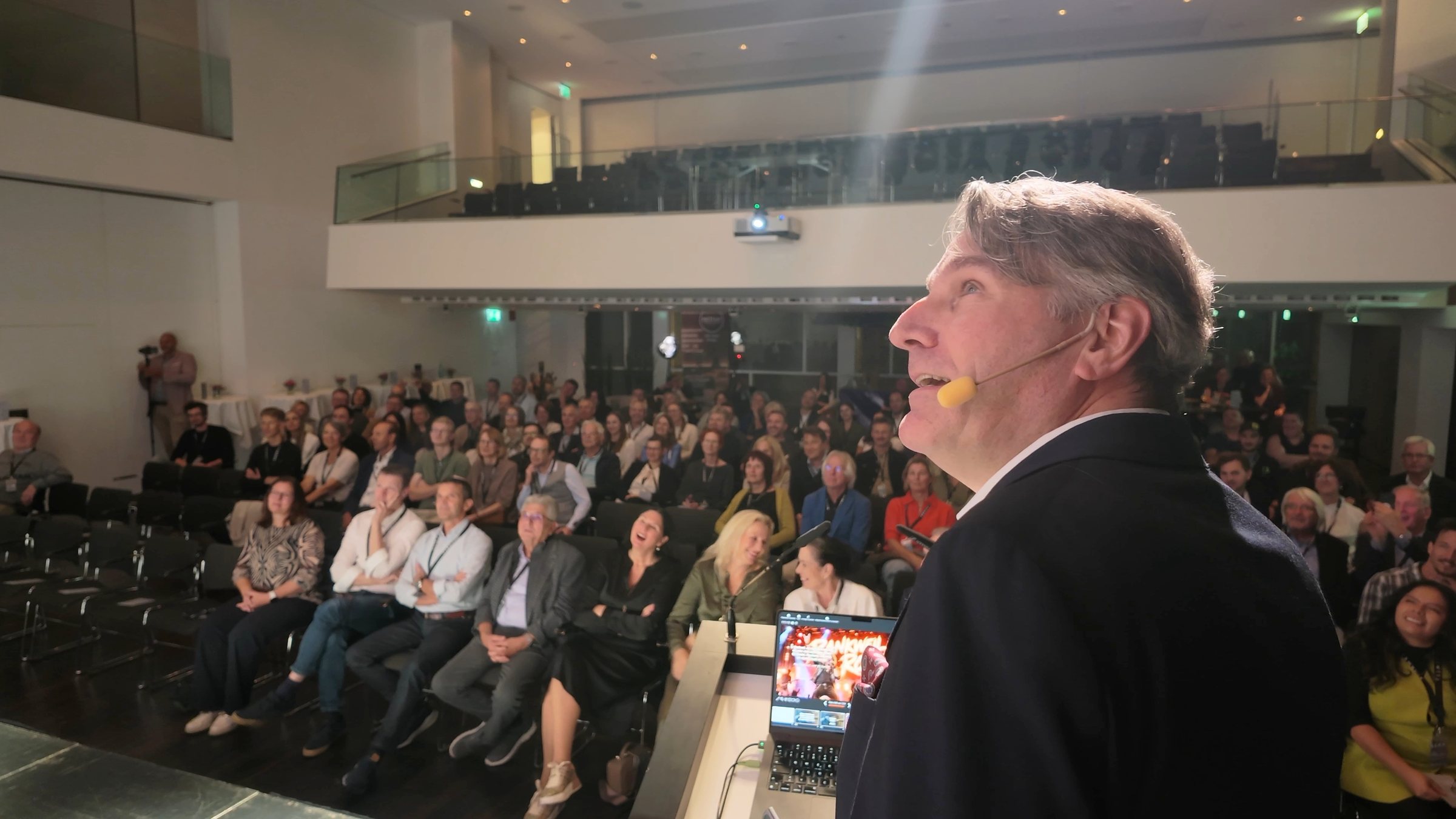 Prof. Dr. Christian Stummeyer auf der Bühne des Vinomnasaals in Rankweil, im Hintergrund das voll besetzte Publikum
