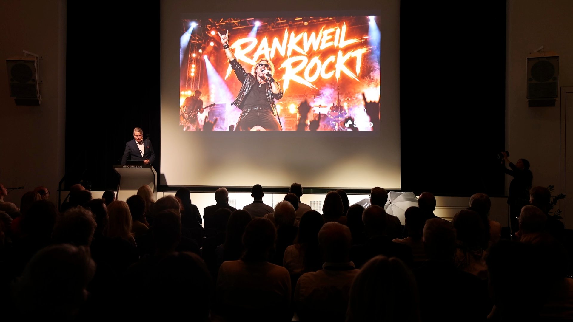 Blick über das Publikum auf die Leinwand mit dem KI-Song „Rankweil rockt“